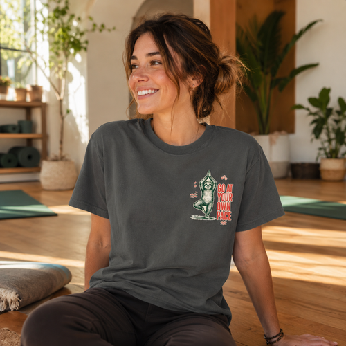 Woman wearing the charcoal Go at Your Own Pace yoga sloth Comfort Colors tee in a sunlit yoga studio