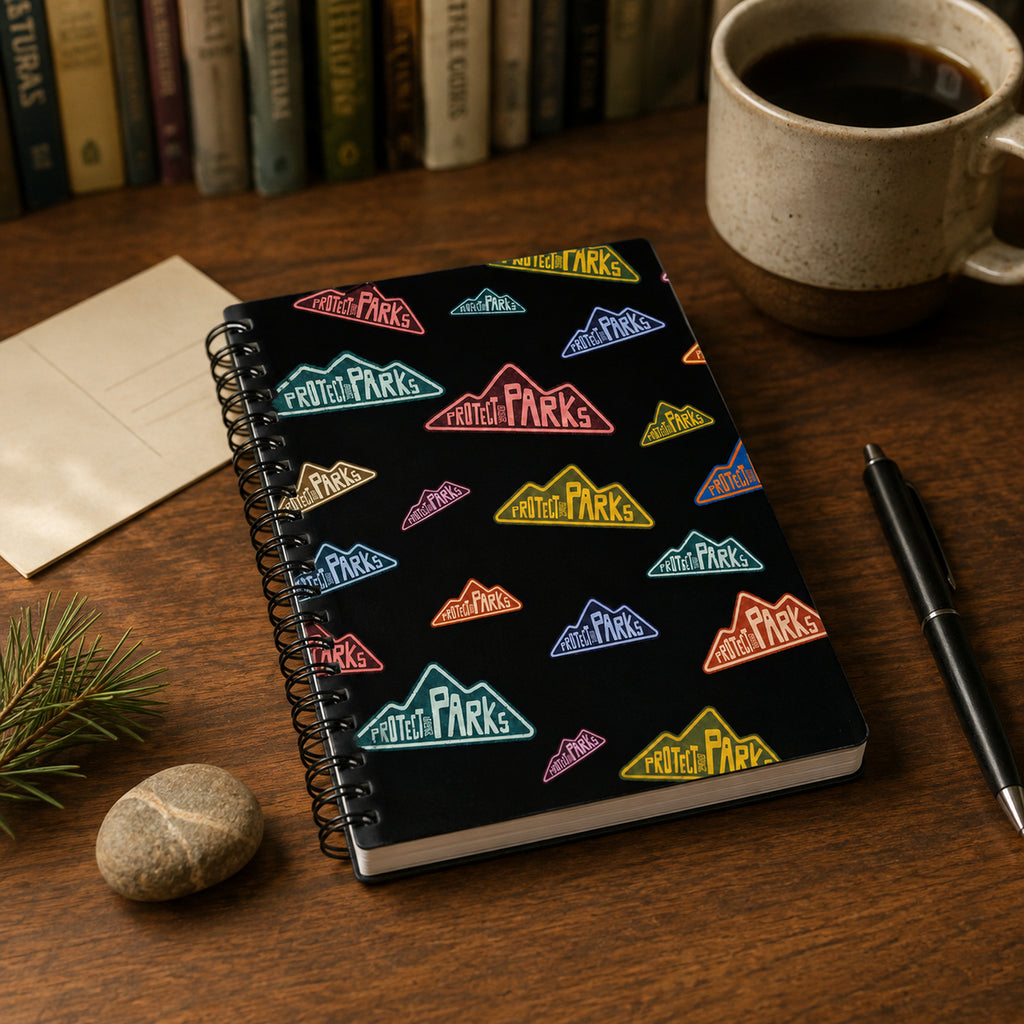 Protect Our Parks black spiral notebook — coffee pine desk scene